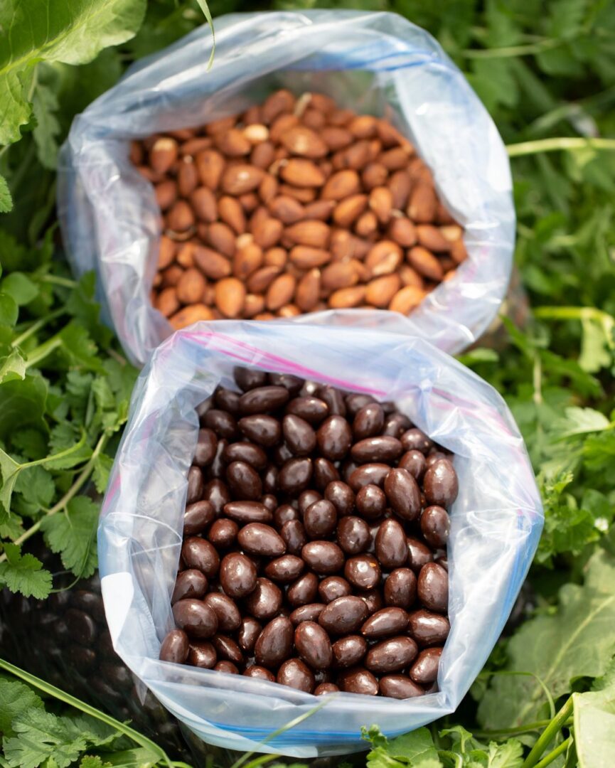 bagged choc and flavored Two bags of beans sitting on top of a bed of green plants.