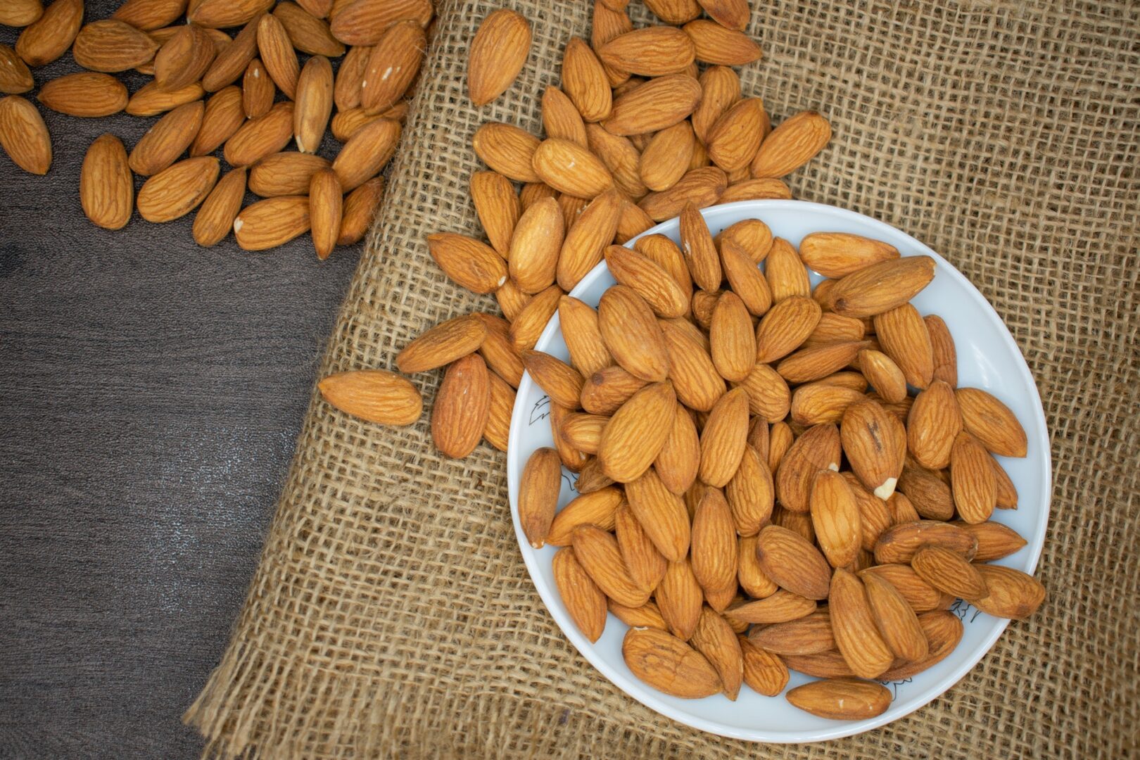 A white plate topped with almonds next to other nuts.